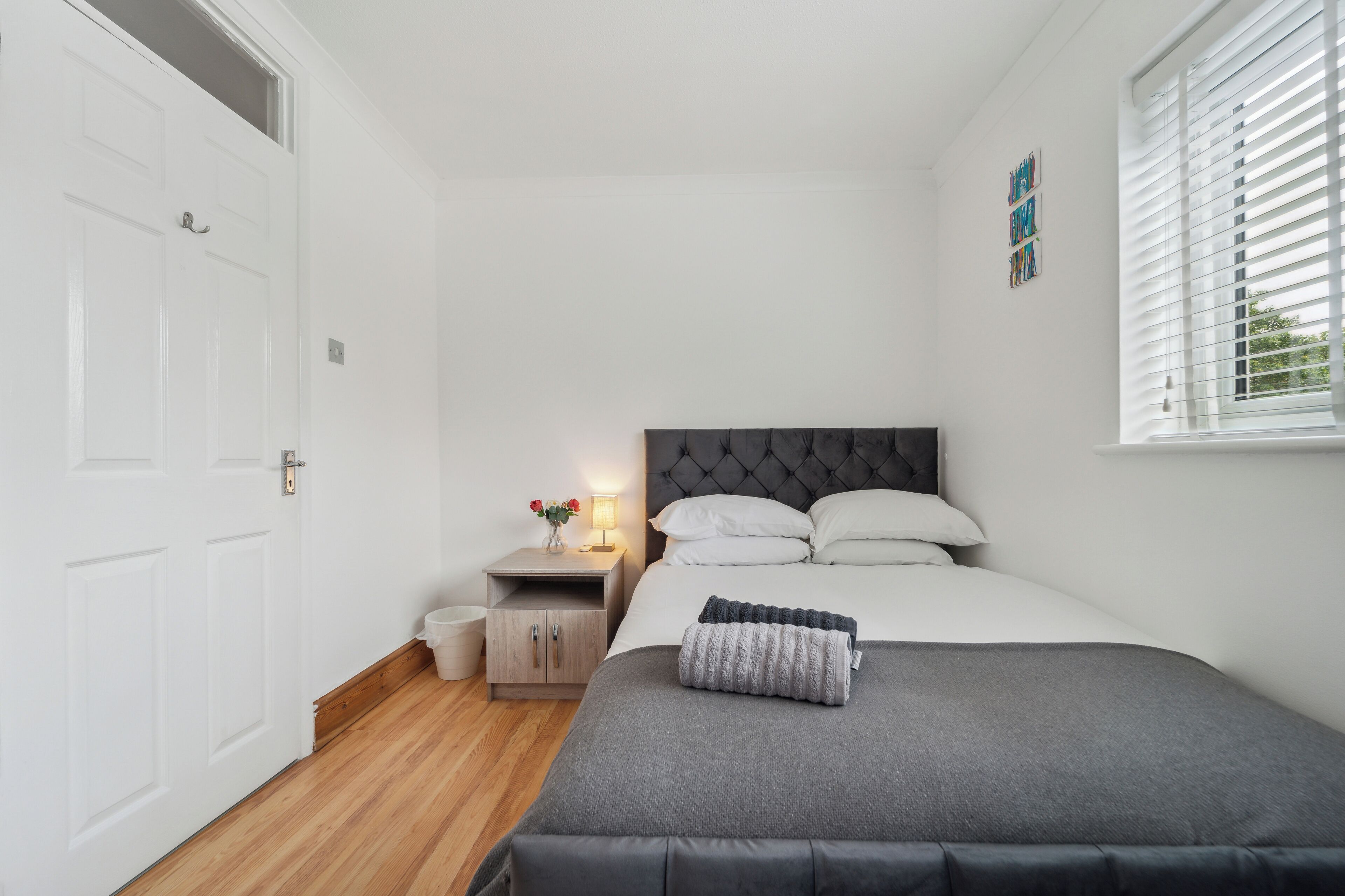A bedroom with a bed, bedside table, and a window with blinds.