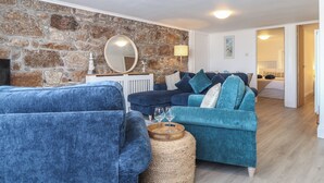 Una sala de estar con una pared de piedra, un espejo redondo, un sofá azul y una mesa de centro de madera.