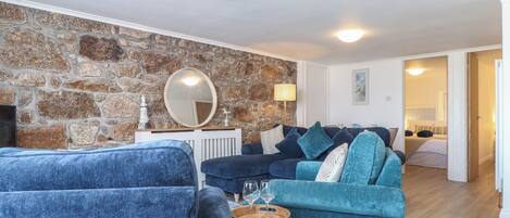 Uma sala de estar com parede de pedra, um espelho redondo, um sofá azul e uma mesa de centro de madeira.