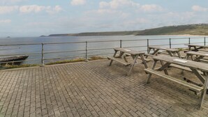 Un paseo marítimo con mesas de picnic y barandilla con vistas al mar.
