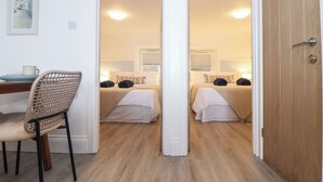 Una habitación de hotel con dos camas, un área de comedor con una silla y un cuadro en la pared.