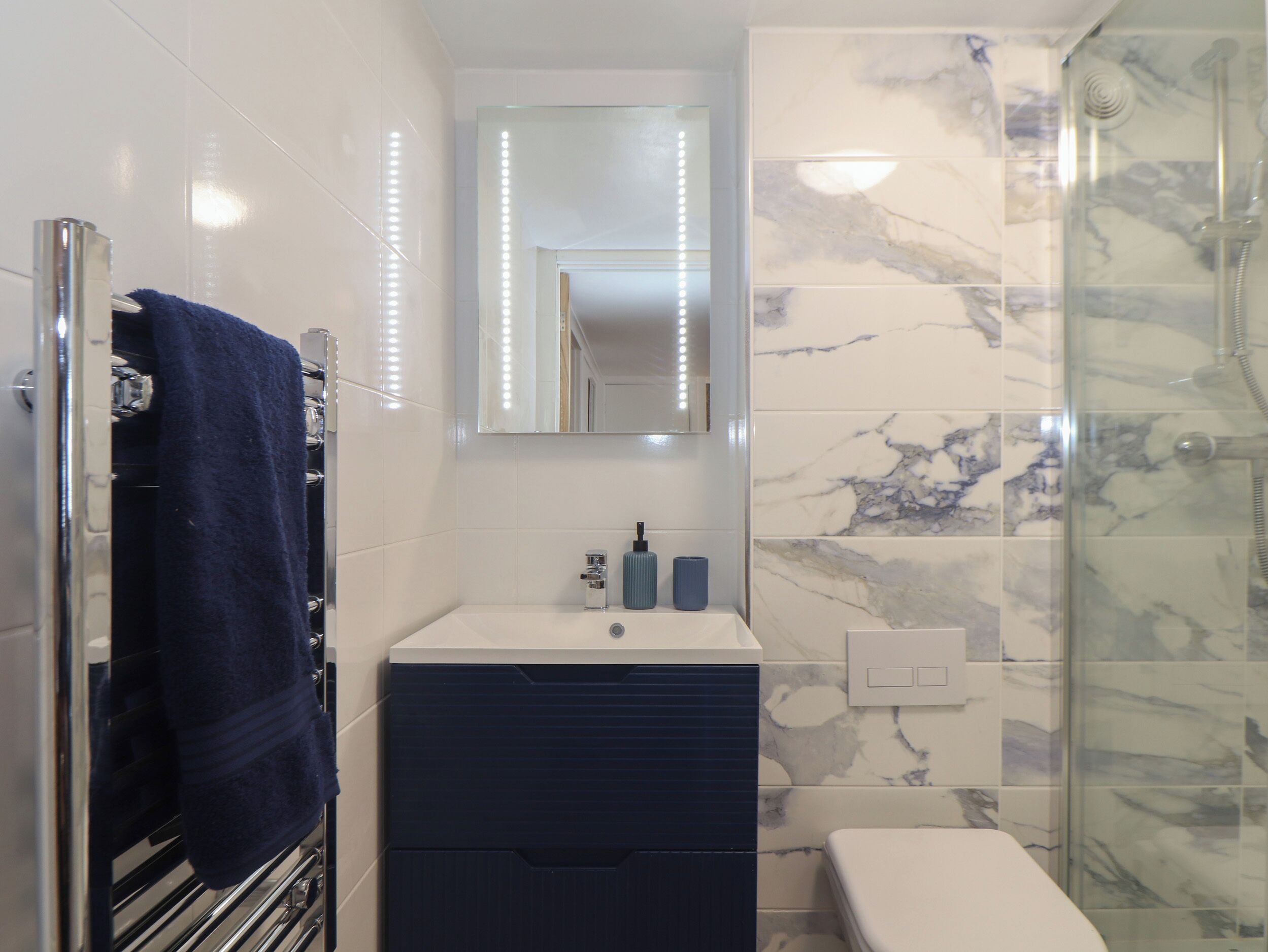 Une salle de bain avec un lavabo blanc, un miroir, un porte-serviettes et un espace douche.