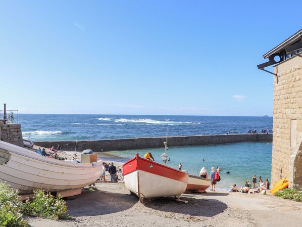 A coastal scene with boats docked at a pier, a stone wall, and people by the water.