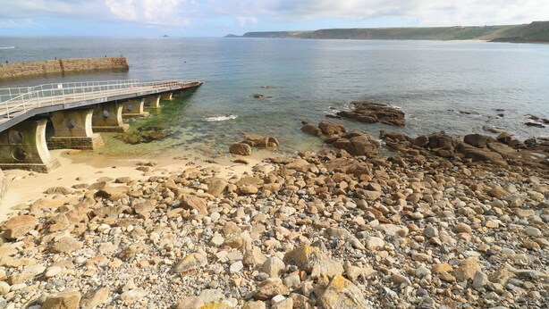 Una playa rocosa con un muelle de piedra que se adentra en el agua.