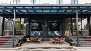 A modern building with a covered outdoor seating area featuring wicker furniture and a fire pit. - Roadside by Khorrot (Tashkent)