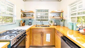 A kitchen with wooden cabinets, a gas stove, a dishwasher, and a window with blinds. - Garden Escape Near Beach, Bikes and BBQ Included (Providenciales)