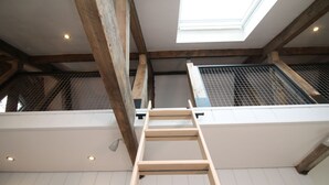 A loft-style room with exposed wooden beams, a skylight, and a metal grid window. - The Hayloft (Crewe)