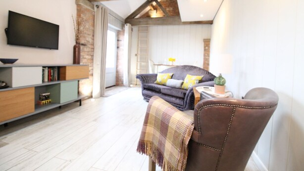 A modern living room with a sofa, a television, and a wooden floor. - The Hayloft (Crewe)