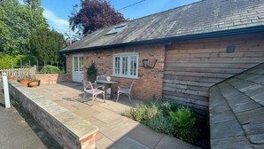 A brick house with a patio, a table, and two chairs. - The Hayloft (Crewe)