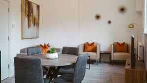 A modern living room with a round dining table, grey sofas, and a small potted plant. - Apartment 7 (York)