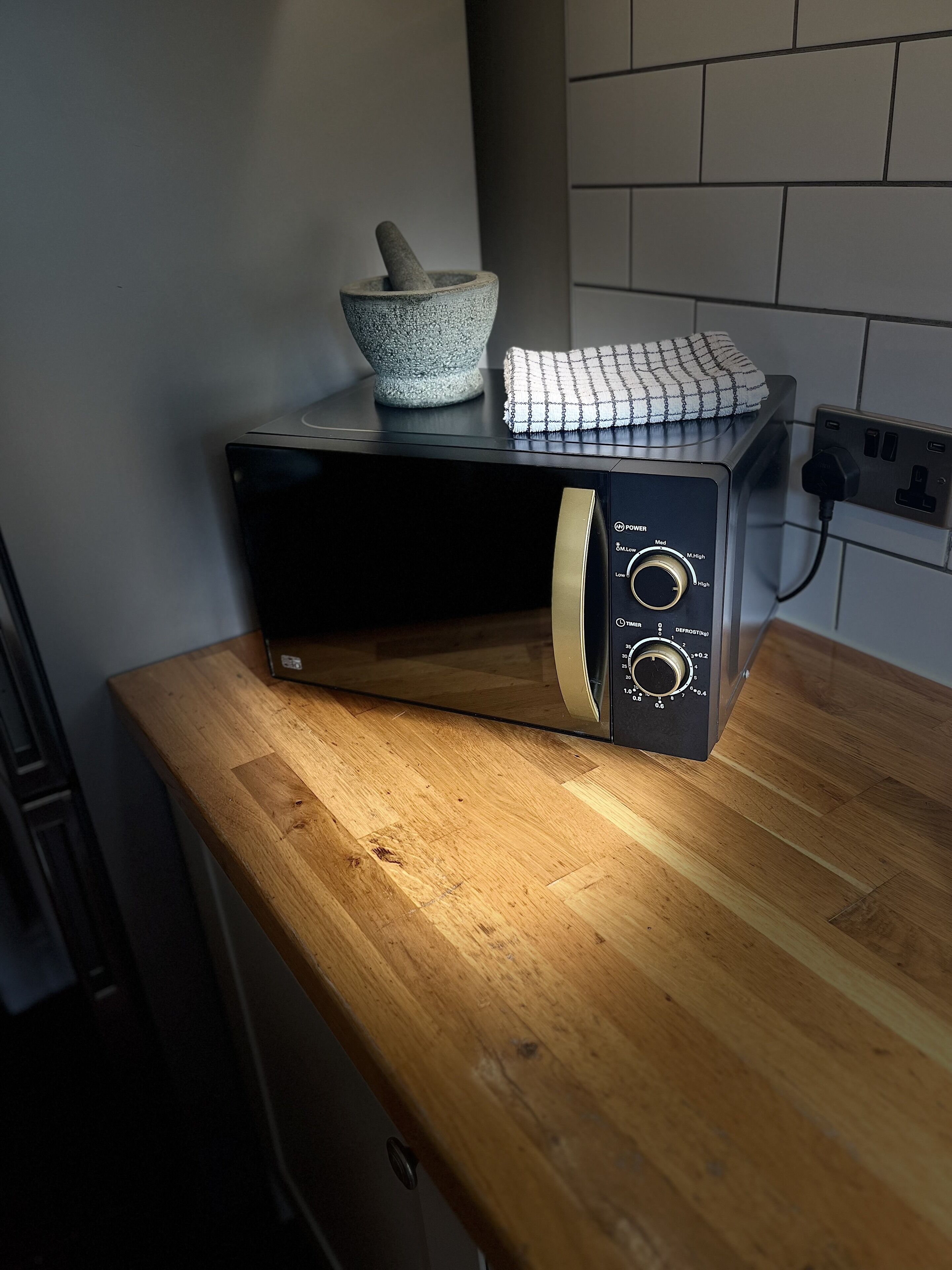 Un four à micro-ondes posé sur un plan de travail en bois, avec une prise de courant et une prise murale à proximité.
