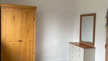 A bedroom with a wooden wardrobe, a dresser with drawers, a bed with a wooden headboard, and a chandelier.