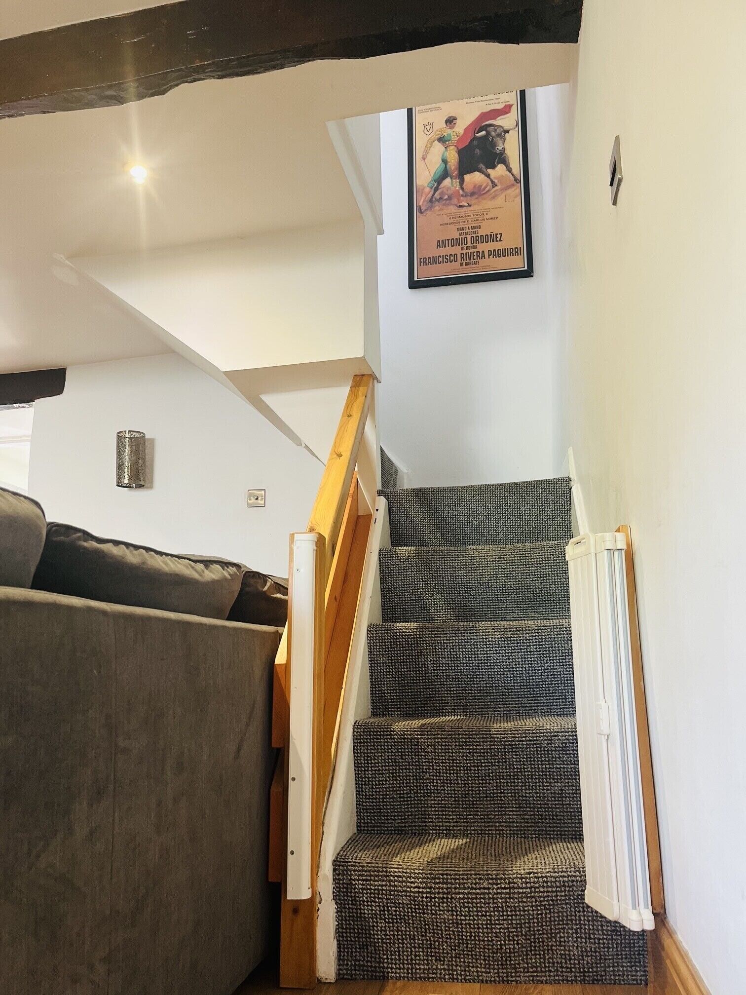 A staircase with a patterned carpet, a wooden handrail, and a black and white poster on the wall.