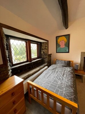 A bedroom with a bed, wooden dresser, stone wall, window, and a painting. - Spring Cottage 2BR Escape - Garden, Coffee Machine, Self Check-in (Trawden)