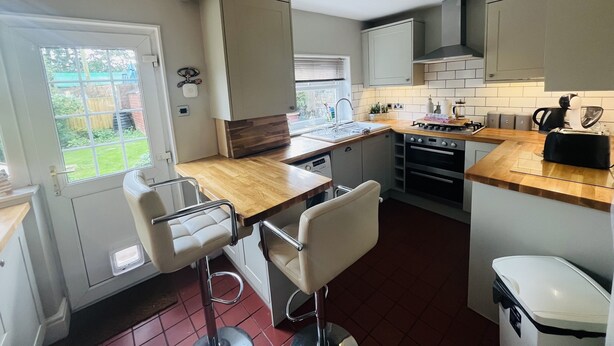 A compact kitchen with a wooden countertop, a sink, a stove, and a trash bin. There is a window with a view of a garden.