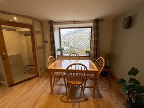 A dining area with a wooden table and chairs, a window with a view, and a door leading to a shower. - Spring Cottage 2BR Escape - Garden, Coffee Machine, Self Check-in (Trawden)