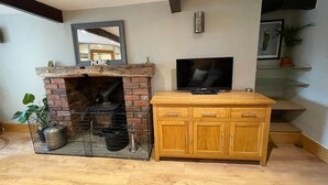 A living room with a brick fireplace, a flat-screen TV, wooden cabinets, and a staircase.
