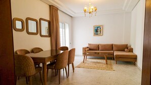 A living room with a dining table, chairs, a sofa, a chandelier, and a painting on the wall. - Ennaser Bliss Your Urban Oasis Awaits (Ariana)