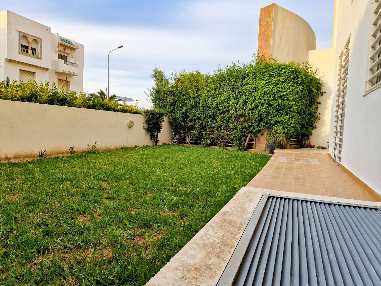 A courtyard with a grassy area, a metal drainage grate, and a wall with a curved structure.