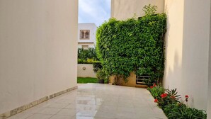 A clean, tiled corridor with a lush green wall on one side and a small garden area with red flowers. - Ennaser Bliss Your Urban Oasis Awaits (Ariana)