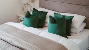 A neatly arranged bedroom with a bed, green pillows, a bedside lamp, and a painting on the wall. - Apartment 8 (York)