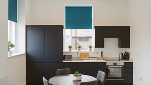 A modern kitchen with dark cabinets, a central island, and a window with a blue blind. - Apartment 8 (York)