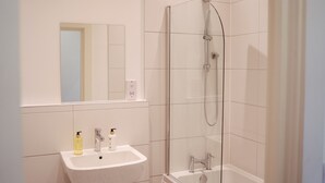 A bathroom with a white sink, two bottles of soap, a mirror, and a glass-enclosed shower with a handheld showerhead. - Apartment 8 (York)
