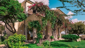 A building with a covered entrance, surrounded by a well-maintained garden with various plants and a clear sky. - The Fantastic Residenza Badus Studio Sleeps 2 Num0828 (Badesi)