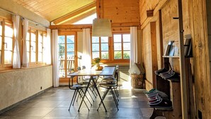 Um quarto espaçoso com teto de madeira alto, uma mesa de jantar com cadeiras, uma janela grande e um sapateiro.