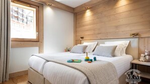 A bedroom with a wooden headboard, a bed with white bedding, a nightstand with a lamp, and a window with curtains. - Wifi, ski-in/ski-out & foot of the slopes, view resort, fitness, swimming pool, sauna, hammam (La Plagne)