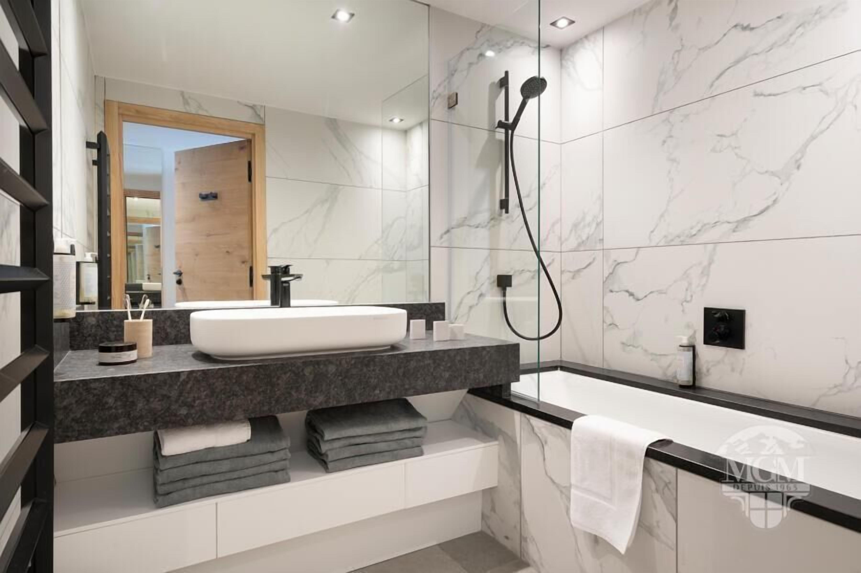 Un baño moderno con un lavamanos blanco, encimera oscura y un espejo grande.