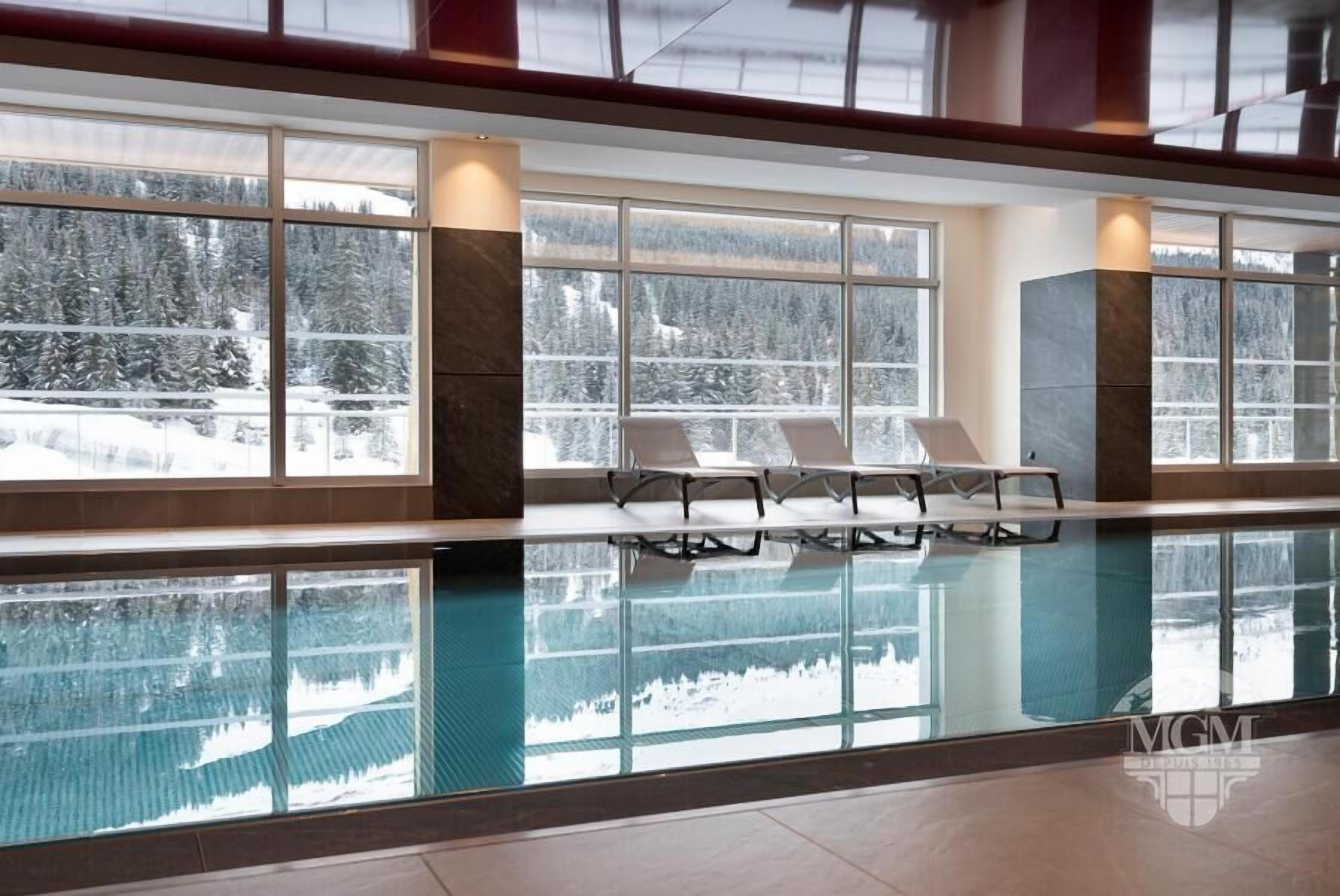 Una piscina interior con paredes de vidrio transparente que reflejan la vista de un bosque nevado.