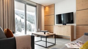 A modern living room with a large window, a flat-screen TV, and a wooden cabinet. - Wifi, ski-in/ski-out & foot of the slopes, view ski slopes, fitness, swimming pool, sauna, hammam (Flaine)