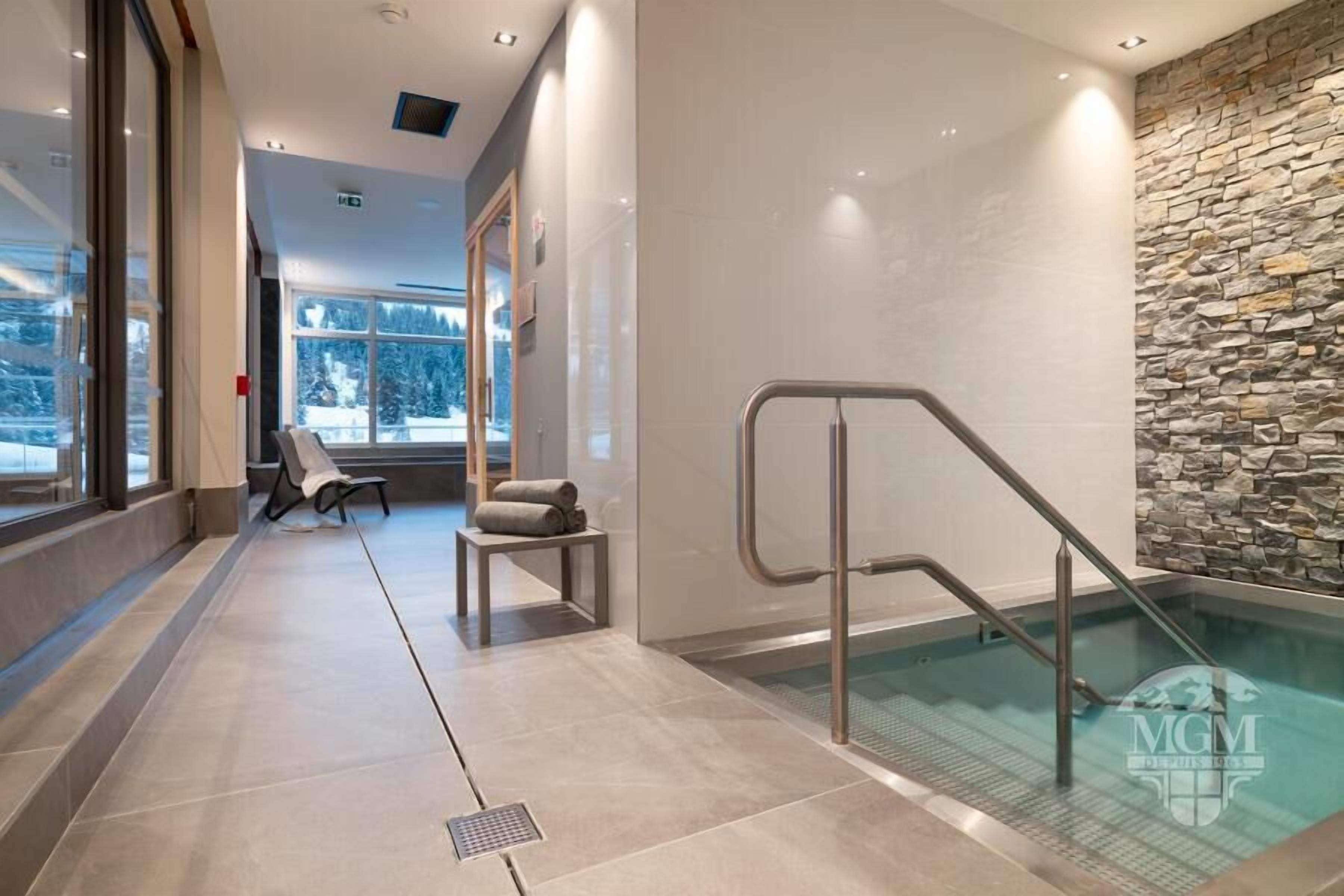 A modern indoor pool area with a stone wall, a glass-enclosed pool, and a chair with towels.