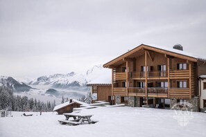 A multi-story wooden lodge with balconies, set against a snowy mountain backdrop. - Wifi, ski-in/ski-out & foot of the slopes, view mountain, fitness, swimming pool, sauna, hammam (Manigod)