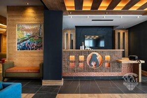 A modern reception area with a wooden reception desk, a large painting, and a seating area with a blue sofa.