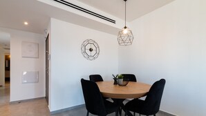 Un comedor moderno con una mesa redonda de madera, sillas tapizadas en negro y dos lámparas colgantes geométricas.