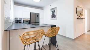 Una cocina moderna con armarios blancos, encimera negra y dos taburetes de mimbre.