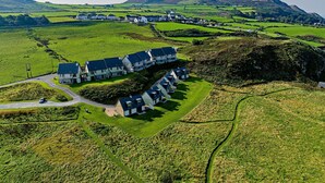 A residential area with houses arranged in a curved layout, surrounded by green fields and hills. - 2 Bed Ground Floor Apartment - 11 (Pwllheli)