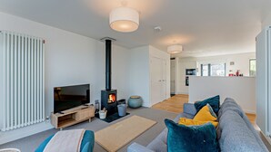 A modern living room with a flat-screen TV, a built-in fireplace, a sofa, and a dining area in the background. - 2 Bed Ground Floor Apartment - 11 (Pwllheli)