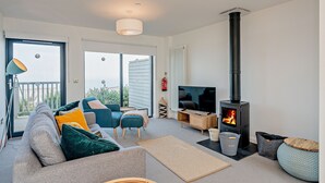 A modern living room with a sofa, chairs, a TV, a fireplace, and a balcony. - 2 Bed Ground Floor Apartment - 11 (Pwllheli)