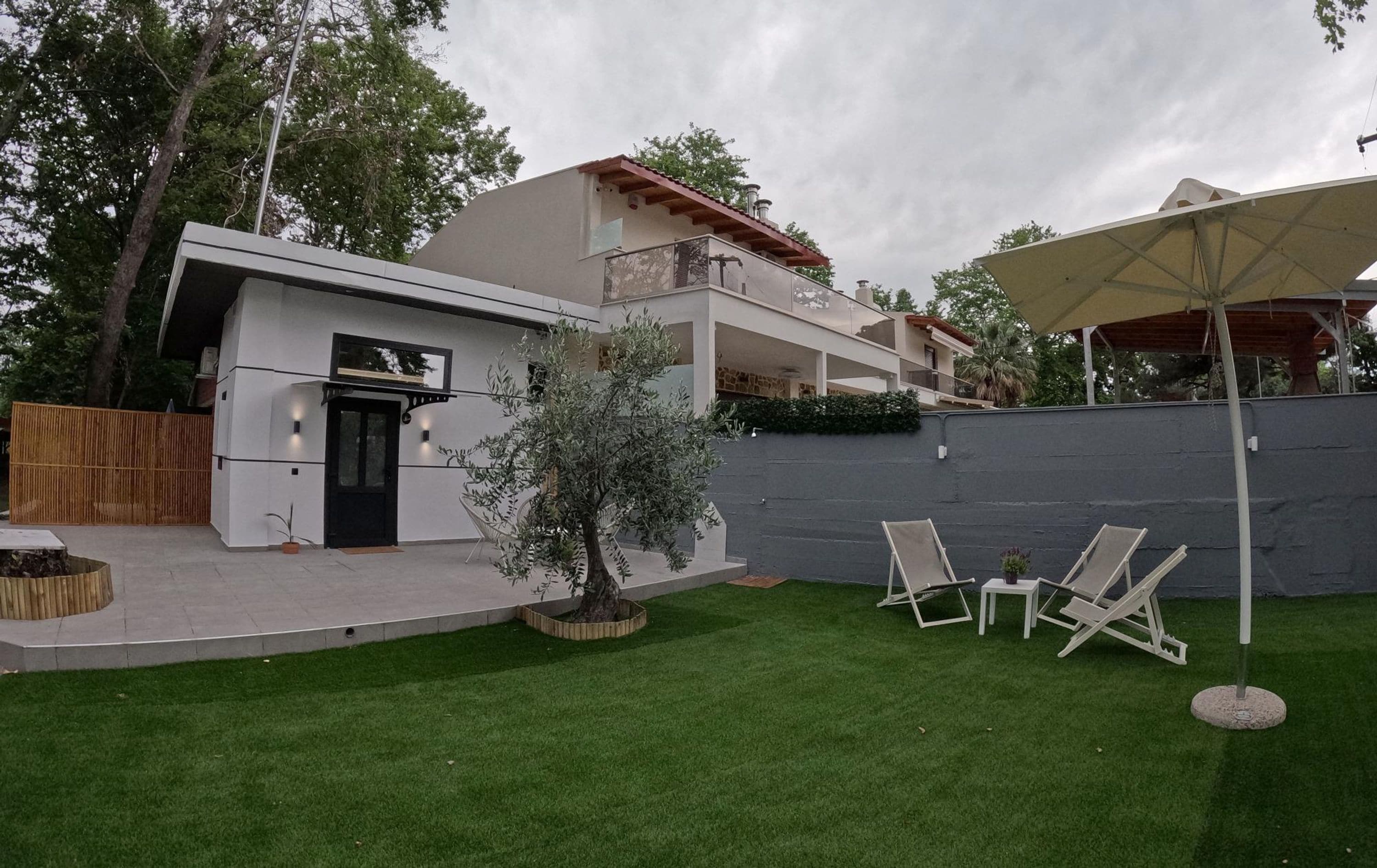 Una casa moderna de dos pisos con un balcón, un pequeño patio con mobiliario exterior y un césped bien cuidado.