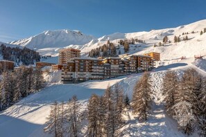A multi-story hotel with a modern architectural design, situated in a snowy mountainous area with ski slopes visible in the background.
