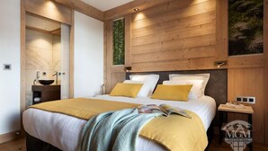 Quarto moderno com cabeceira de madeira, uma cama grande com roupa de cama amarela, mesa de cabeceira com abajur e um espelho.