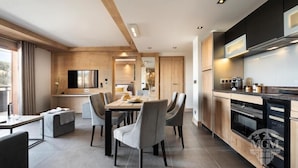 A modern kitchen with wooden cabinets, a dining area with grey chairs, and a built-in TV. - Wifi, ski-in/ski-out & foot of the slopes, view mountain, fitness, swimming pool, sauna, hammam (La Plagne)