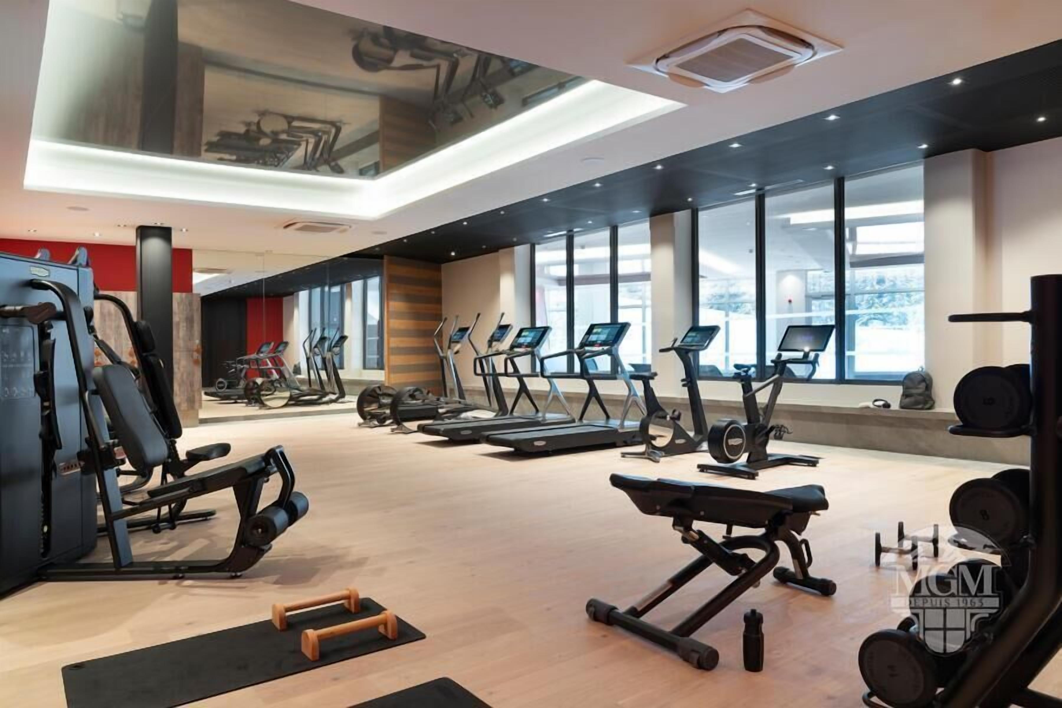 Een moderne sportschool met diverse fitnessapparaten, grote ramen en een houten vloer.