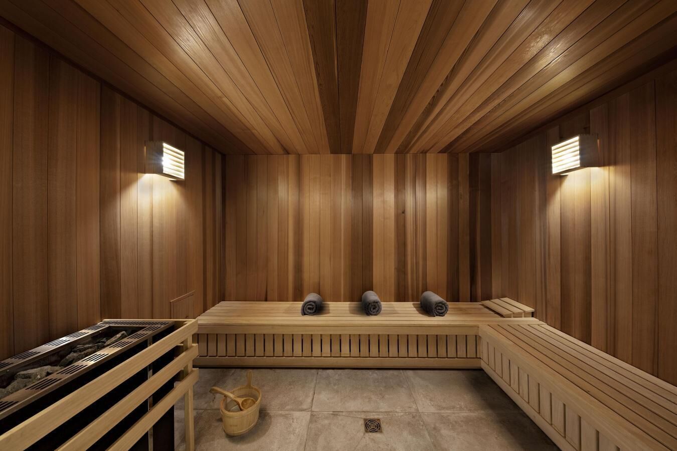 Ein Saunaraum mit Holzwänden und -bänken, einem Steinfußboden und einem Holz-Eimer.