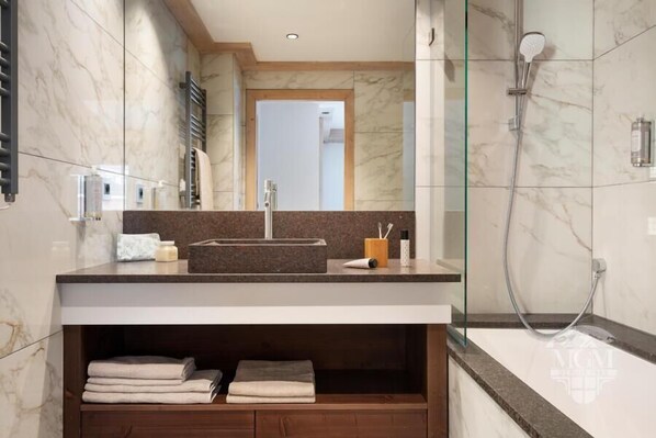 A modern bathroom with a marble vanity, a glass shower enclosure, and a built-in shelf with towels. - Wifi, 300m from resort center, Ground floor, view mountain/resort, fitness, swimming pool, sauna (La Plagne)