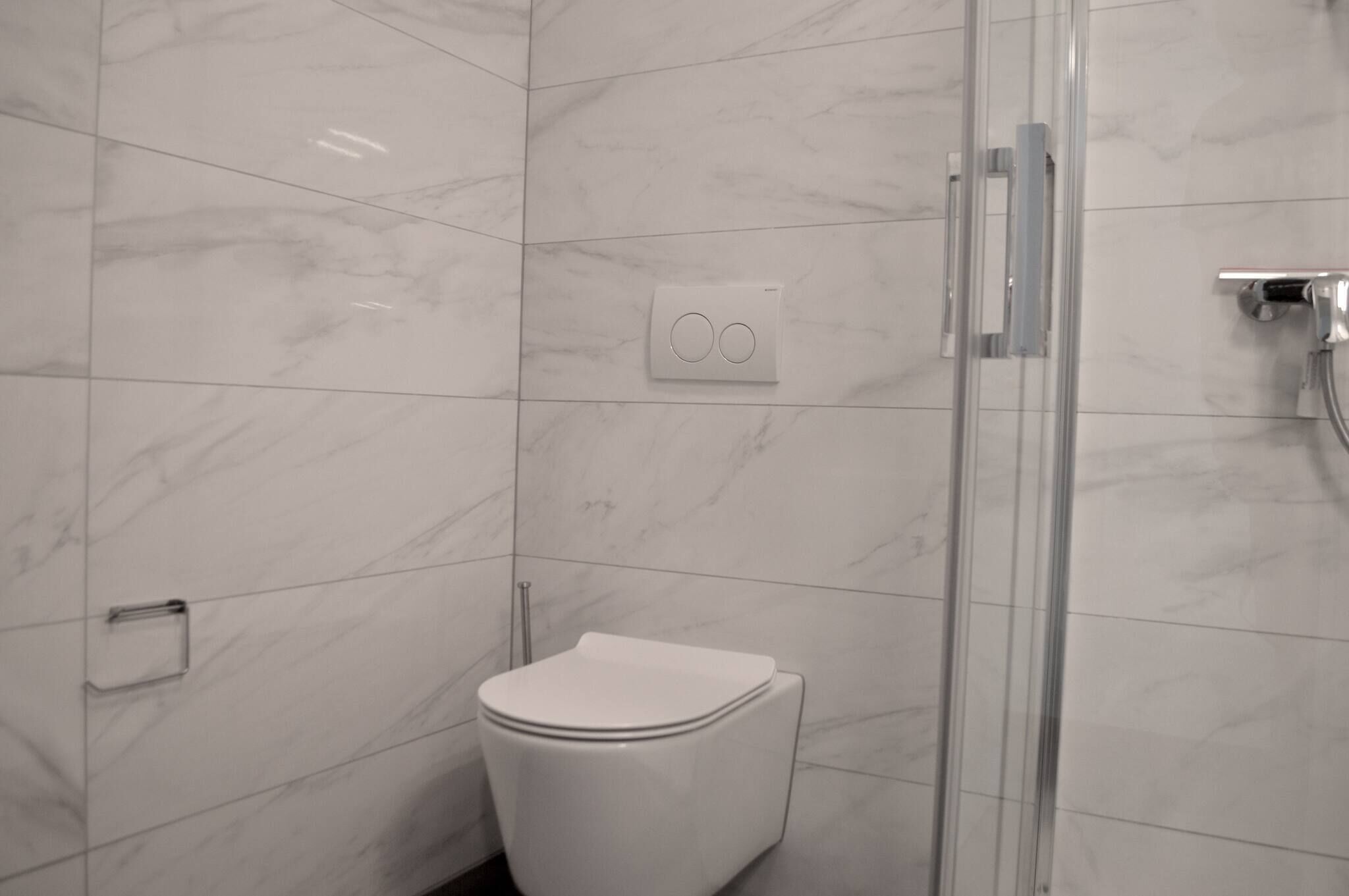Un bagno con un water bianco, cabina doccia in vetro e pannello di controllo a parete.