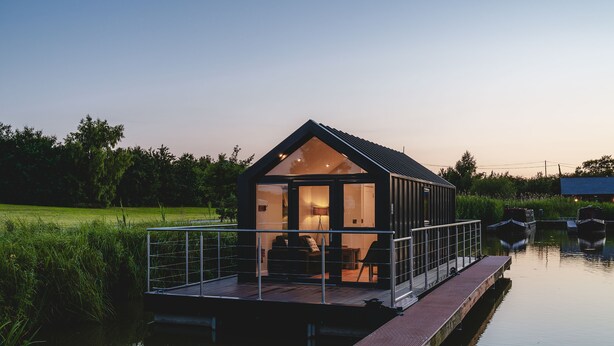 Una moderna casa flotante con fachada de vidrio, terraza y una pequeña zona de estar al aire libre.